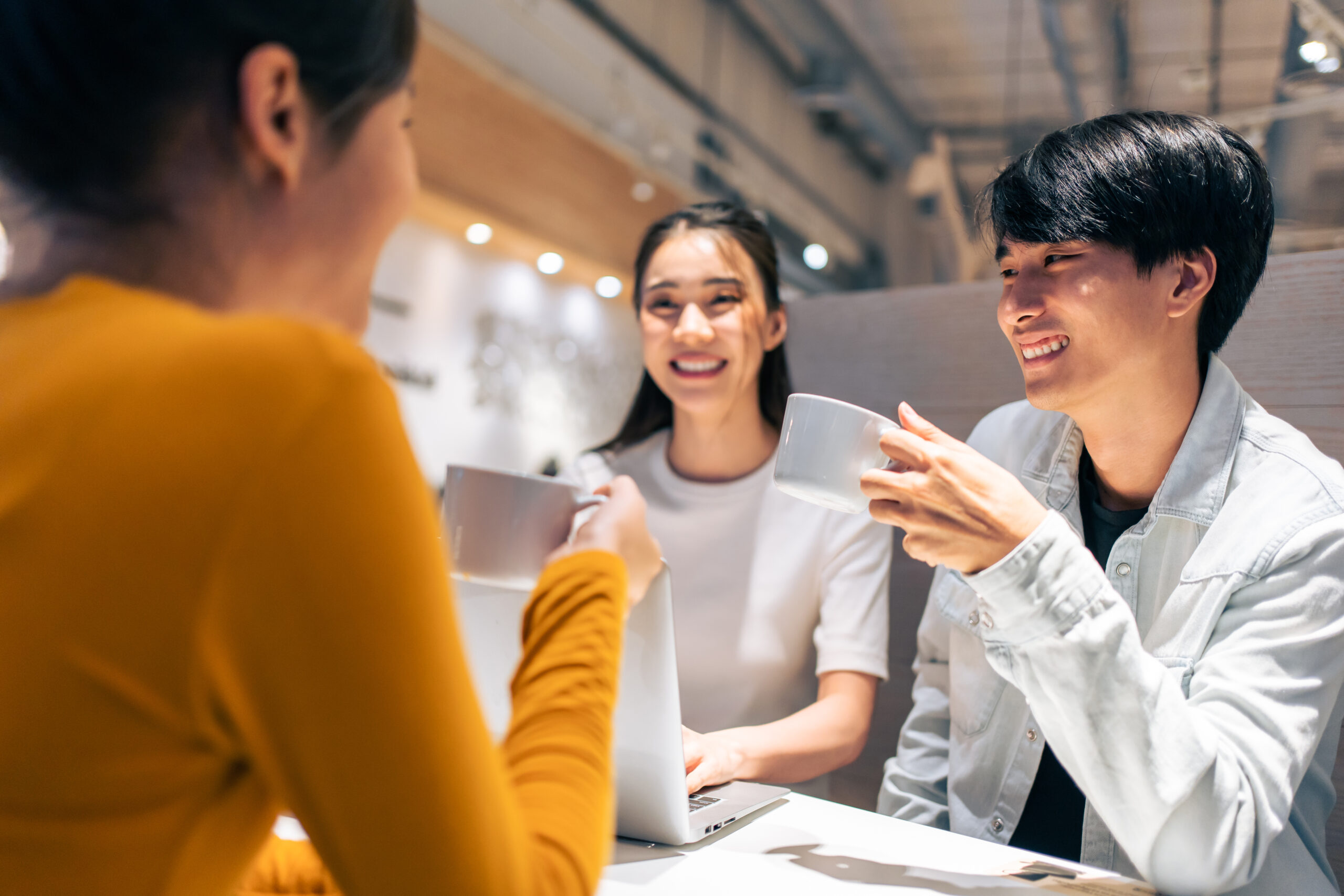 Group of Asian friends talking and using laptop computer in restaurant. Attractive young man and woman people feel happy and relax, having fun hangout indoors enjoy meeting reunion in cafe cafetaria.